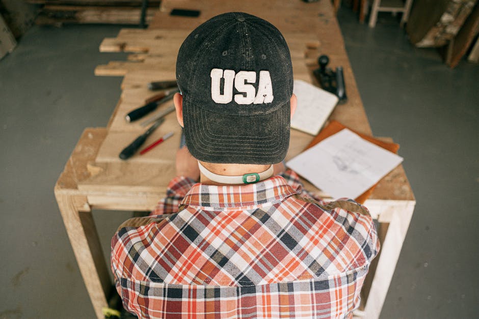 A male carpenter working on wood projects in a rustic workshop, viewed from behind.