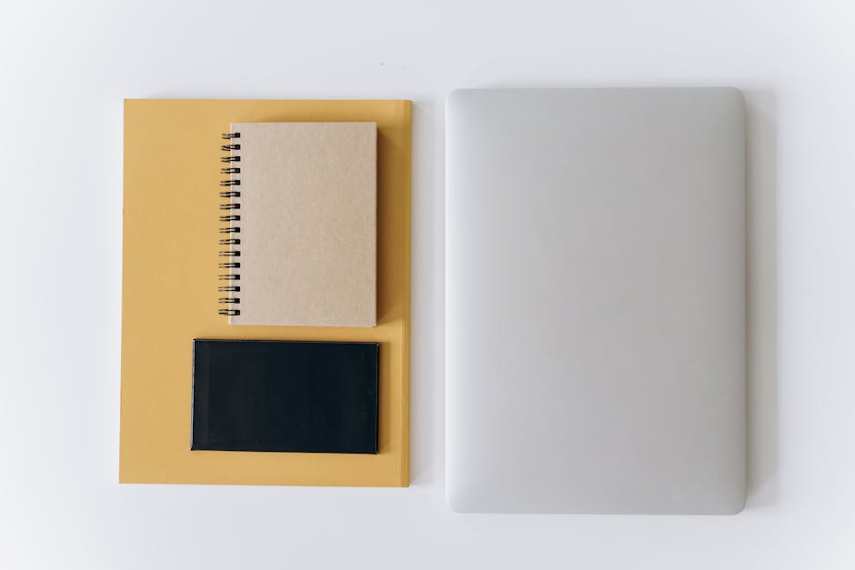 Flat lay of a closed laptop, notebook, and tablet on neutral surface.