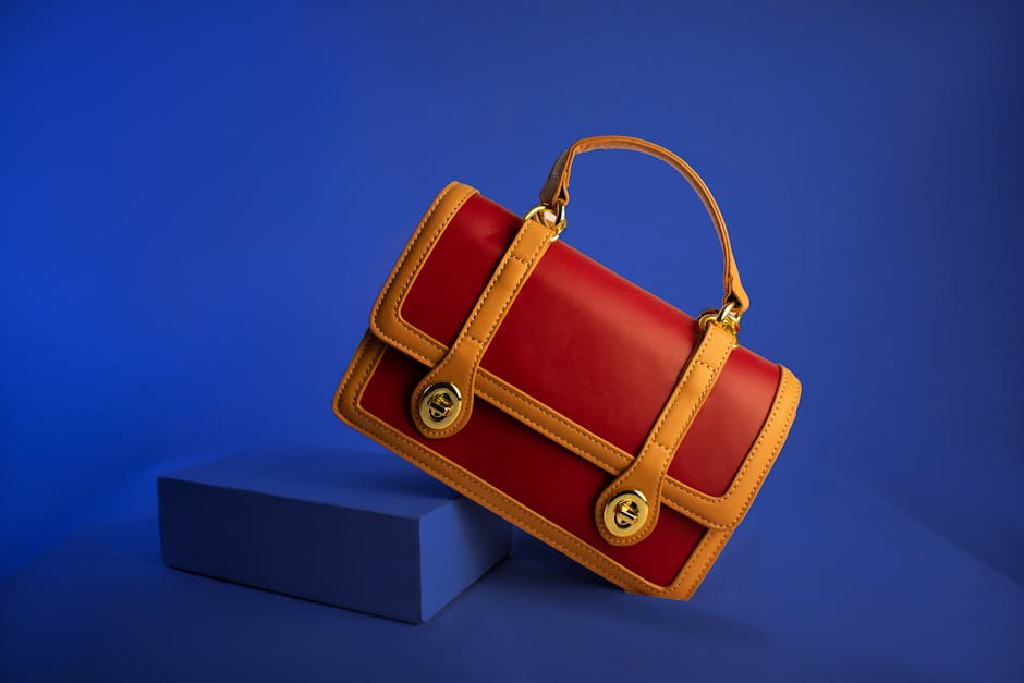Stylish red and tan leather handbag with handle and gold accents on vibrant blue backdrop.