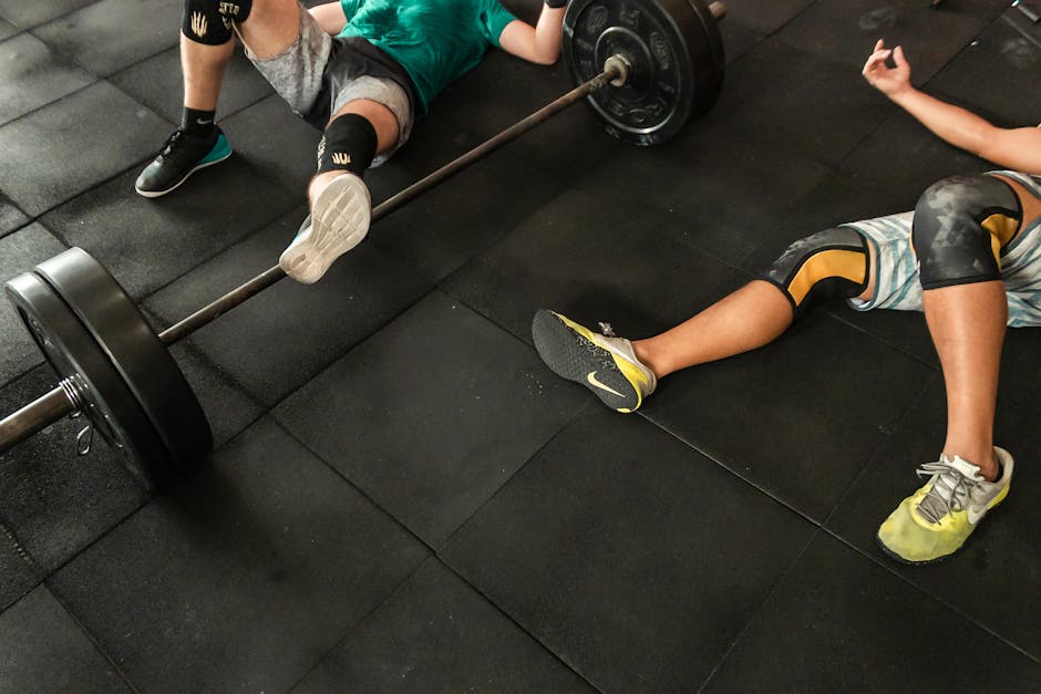 Athletes resting on a gym floor beside heavy barbells after an intense weightlifting session.