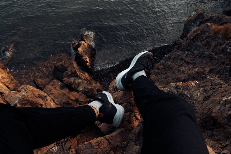 Shoes dangle over rocky cliff edge overlooking the sea, suggesting adventure.