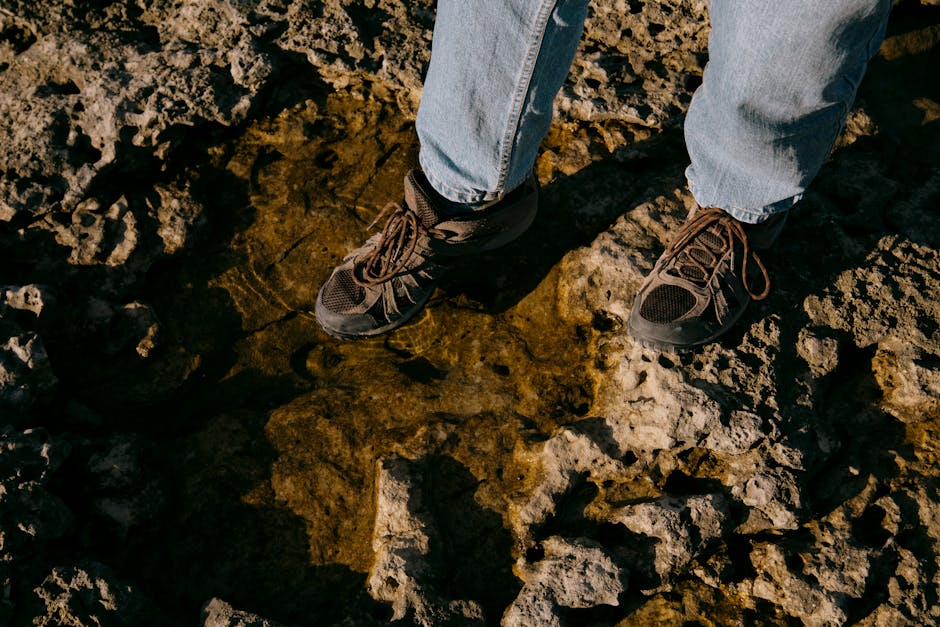A hiker standing on rocky ground with water puddles, wearing casual shoes and jeans.